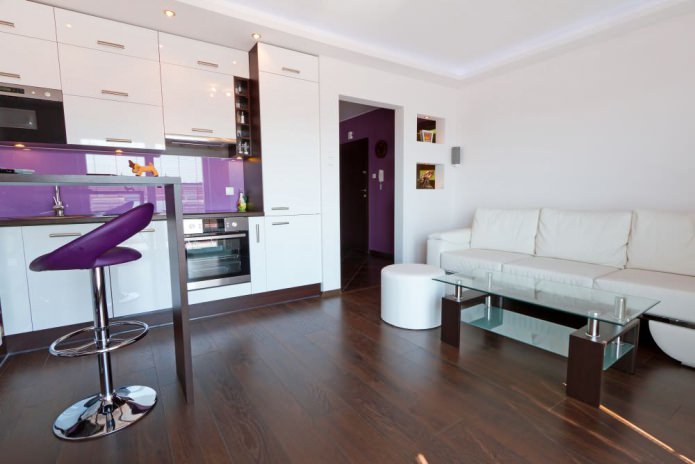 Keittiö-olohuone, jossa baaritiski valkoisilla ja violeteilla sävyillä