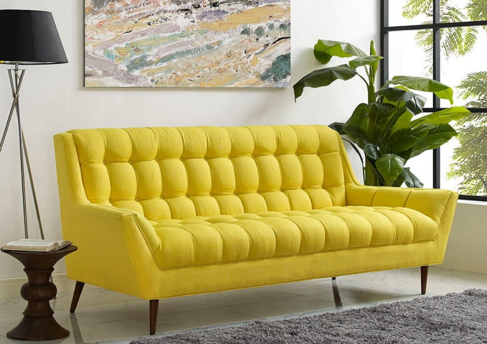dzeltens dīvāns uz kājām interjerā