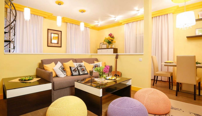šviesiai geltona svetainė su įvairiaspalvėmis pagalvėmis ir megztais pufais