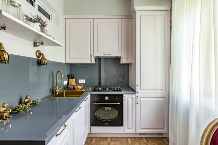 bucătărie mică cu mobilier alb, blaturi gri și un șorț din același material